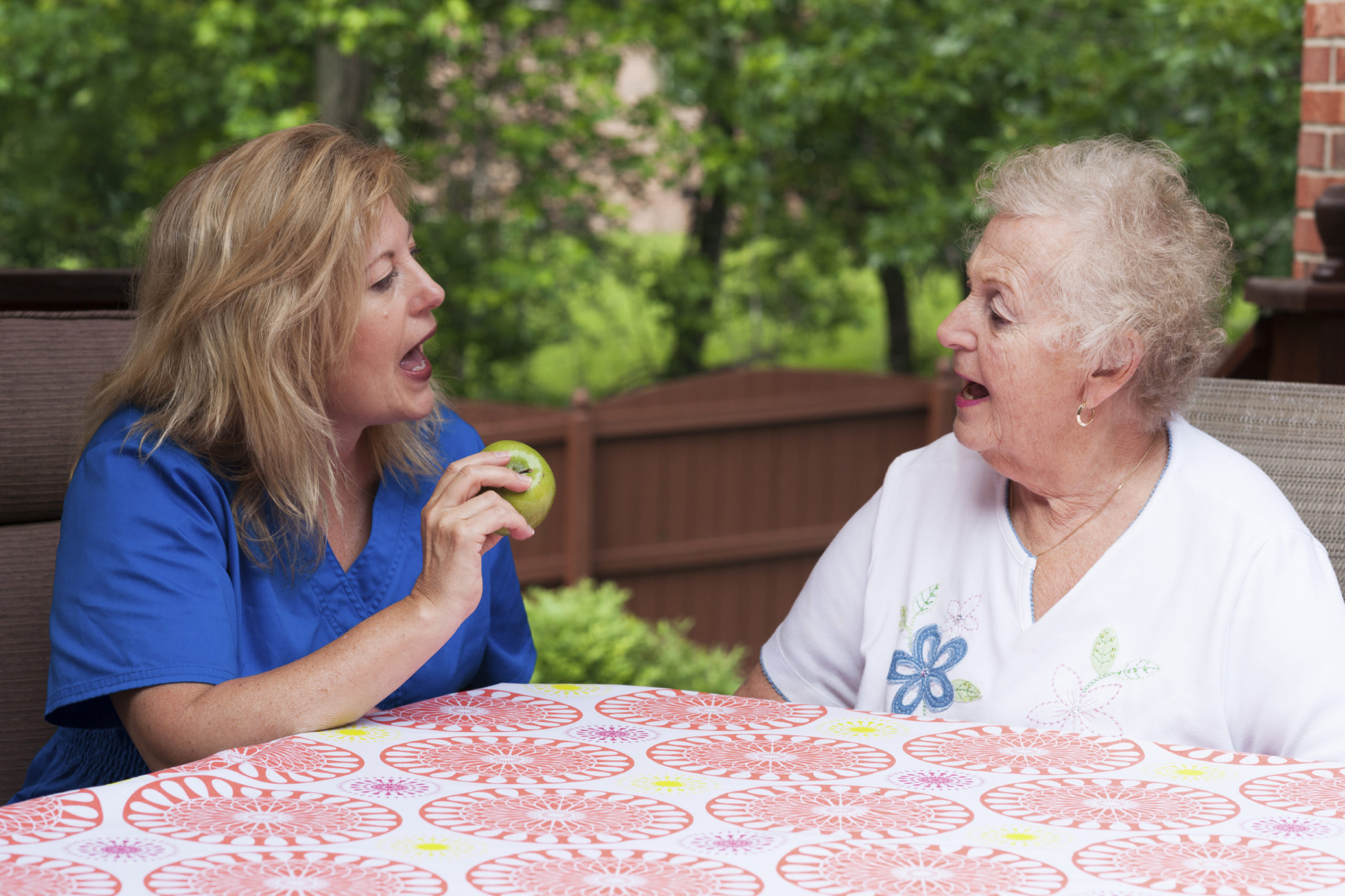 Speech therapist with female stroke patient outdoors during a home health therapy session modeling the production of a consonant during speech training for apraxia